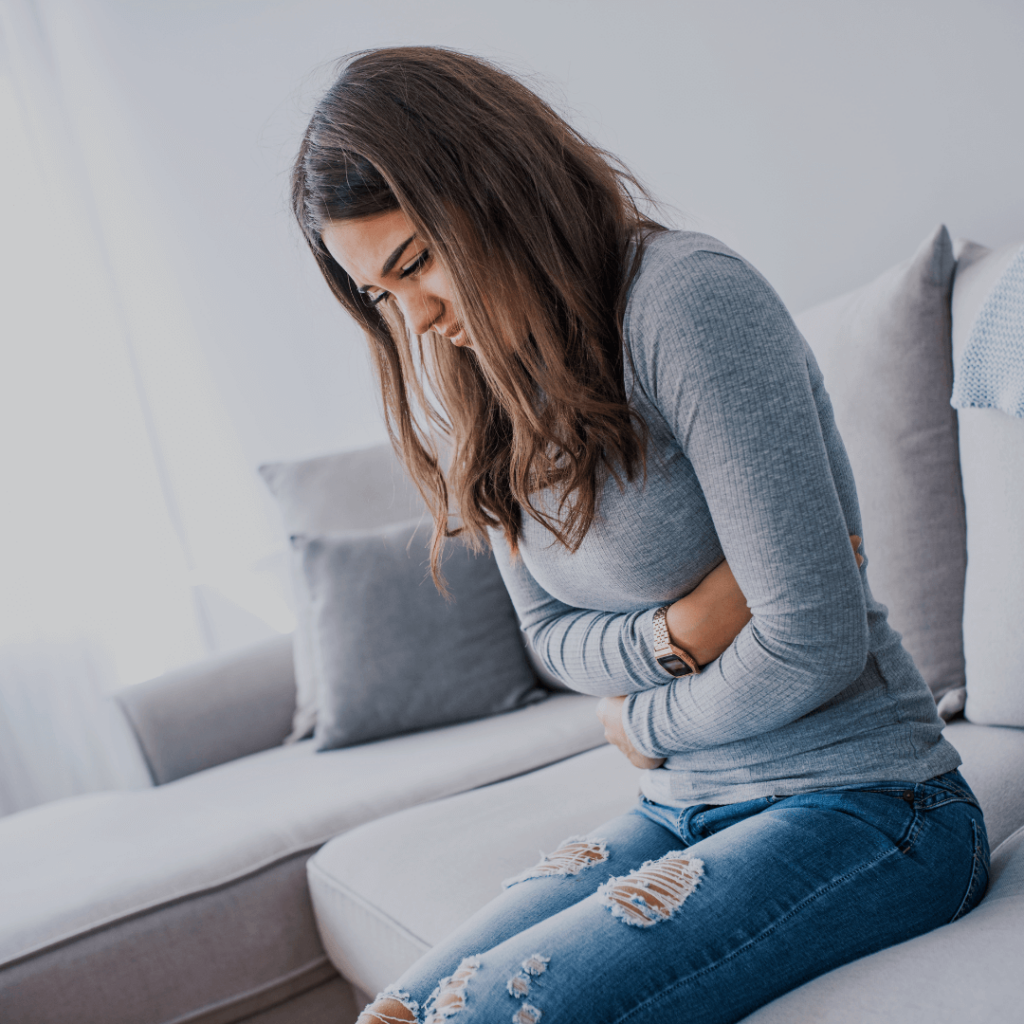 Woman feeling pit in stomach on couch to show physical signs of anxiety